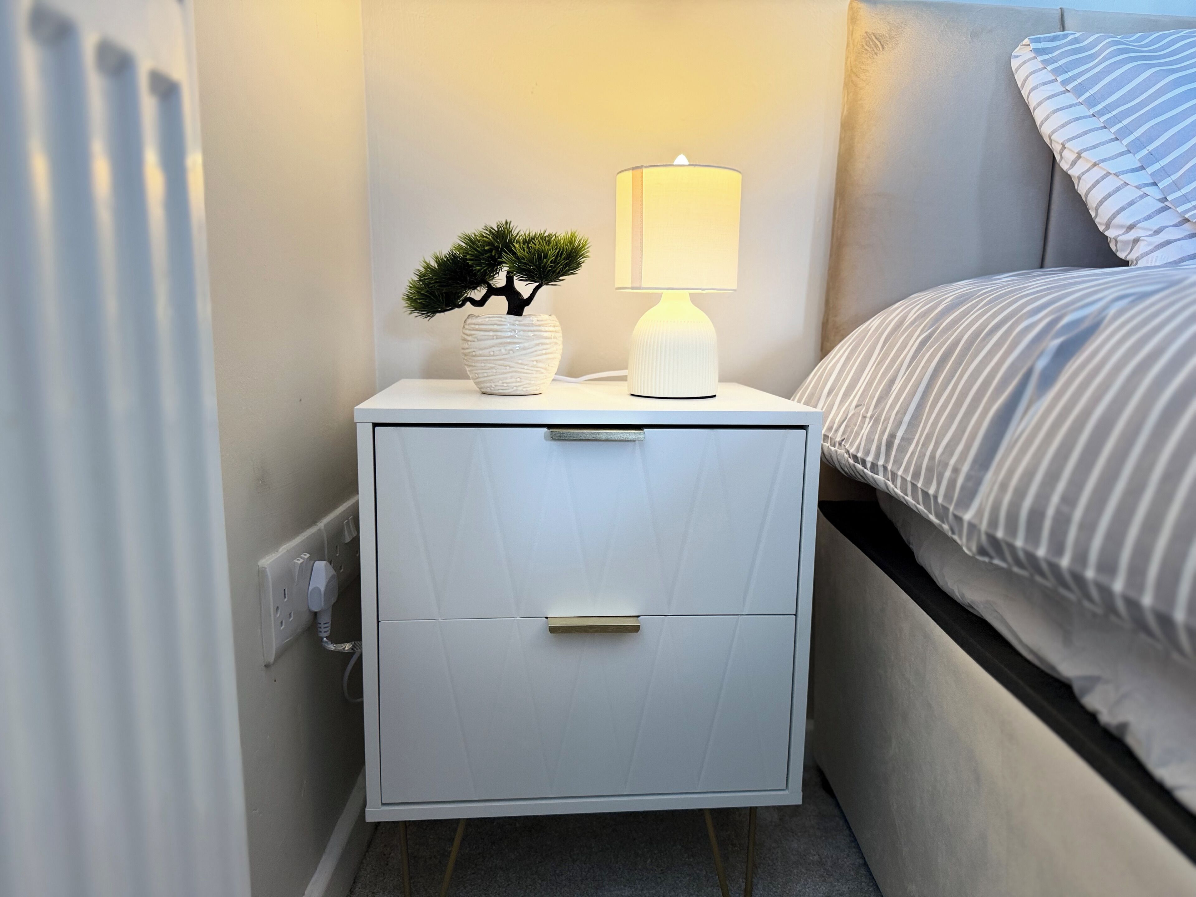 A white bedside table with a lamp and a small potted plant.