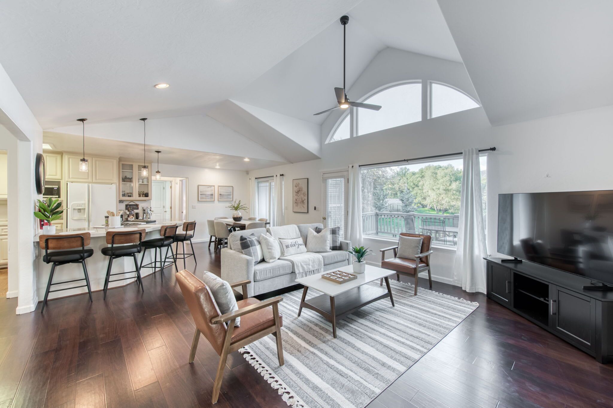 A spacious living area with a large window, a ceiling fan, and a kitchen area with modern appliances.