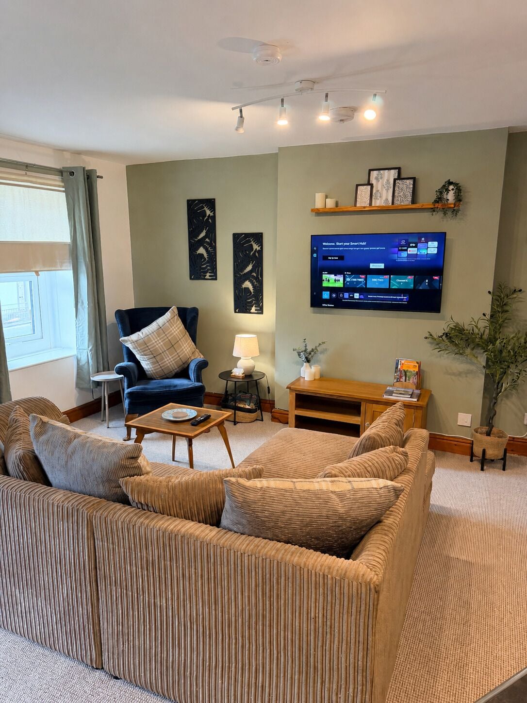 A living room with a sofa, armchair, coffee table, lamp, TV, and decorative items.