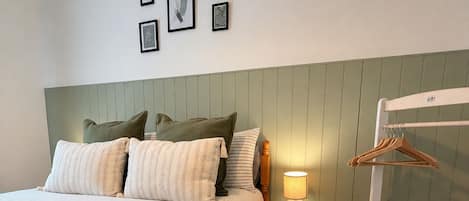 A neatly made bed with pillows, a bedside lamp, and a wooden hanger rack.