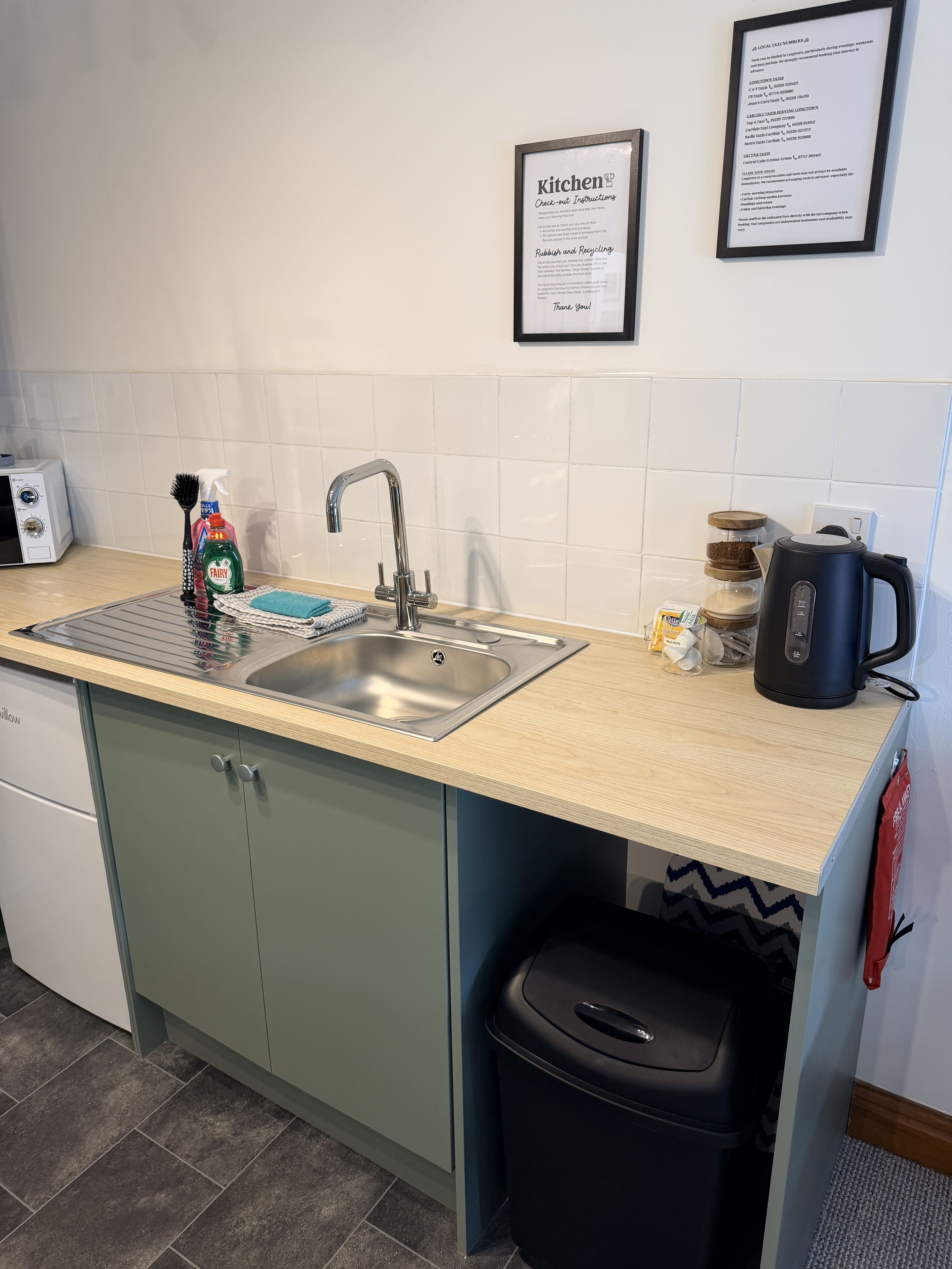 Una cocina con un lavamanos, una cafetera y un bote de basura.