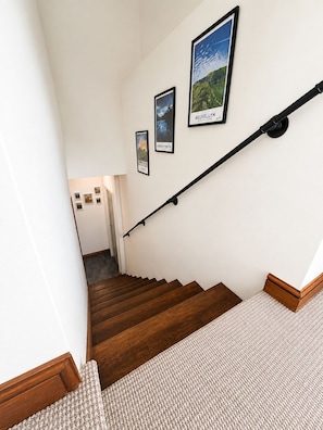 A staircase with wooden steps and a handrail, leading to a landing with framed pictures on the wall.