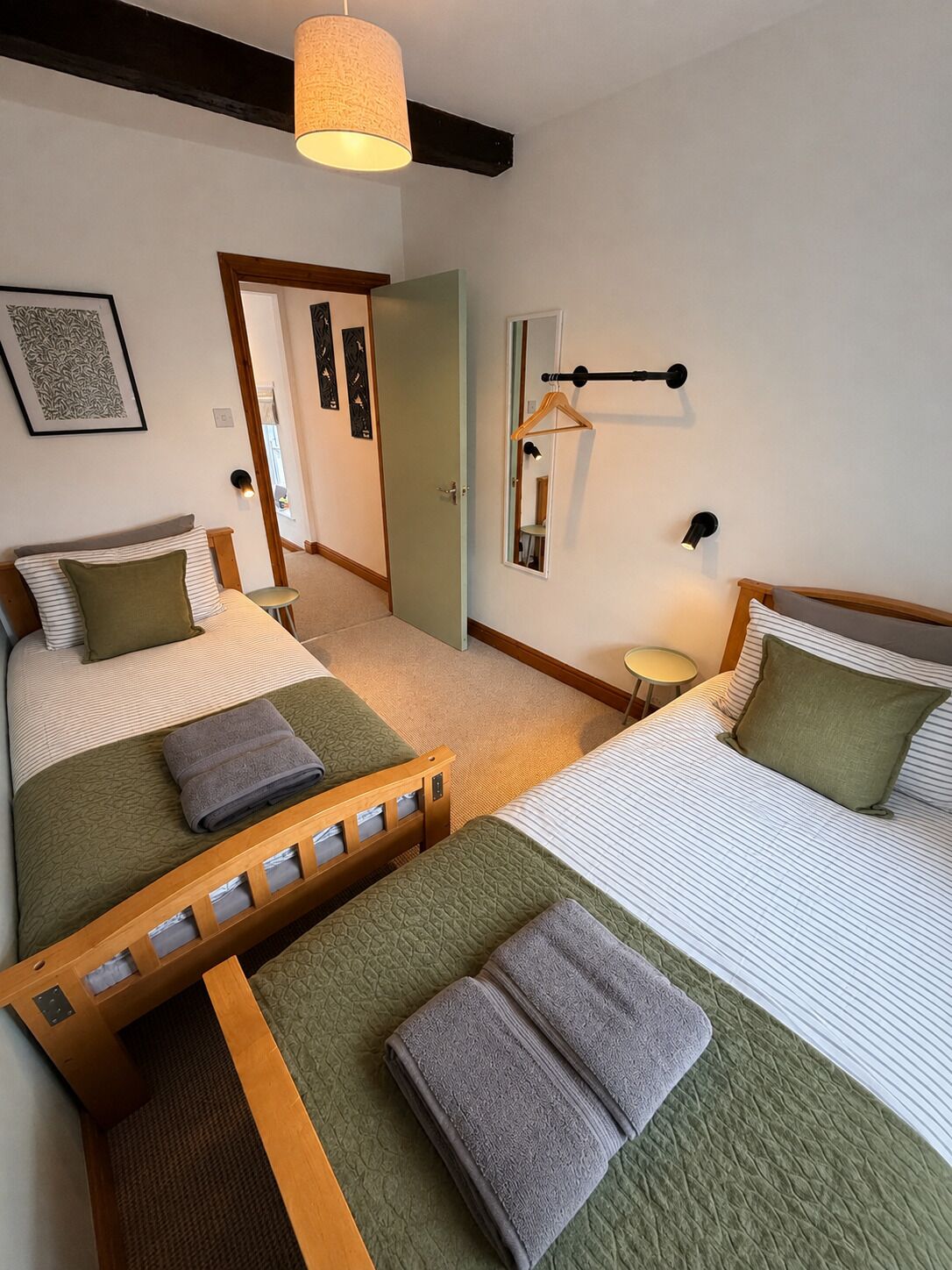 Een hotelkamer met twee bedden, een nachtkastje, een hanglamp, een spiegel en een deur naar een andere kamer.