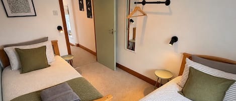 A hotel room with two beds, a bedside table, a hanging light fixture, a mirror, and a door leading to another room.