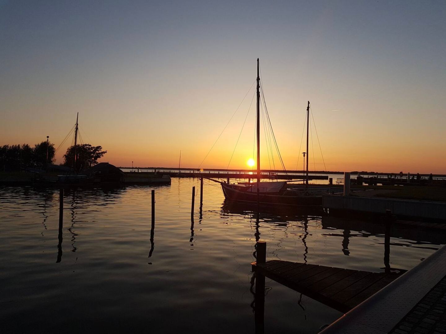 A calm waterfront at sunset with a dock and a boat.