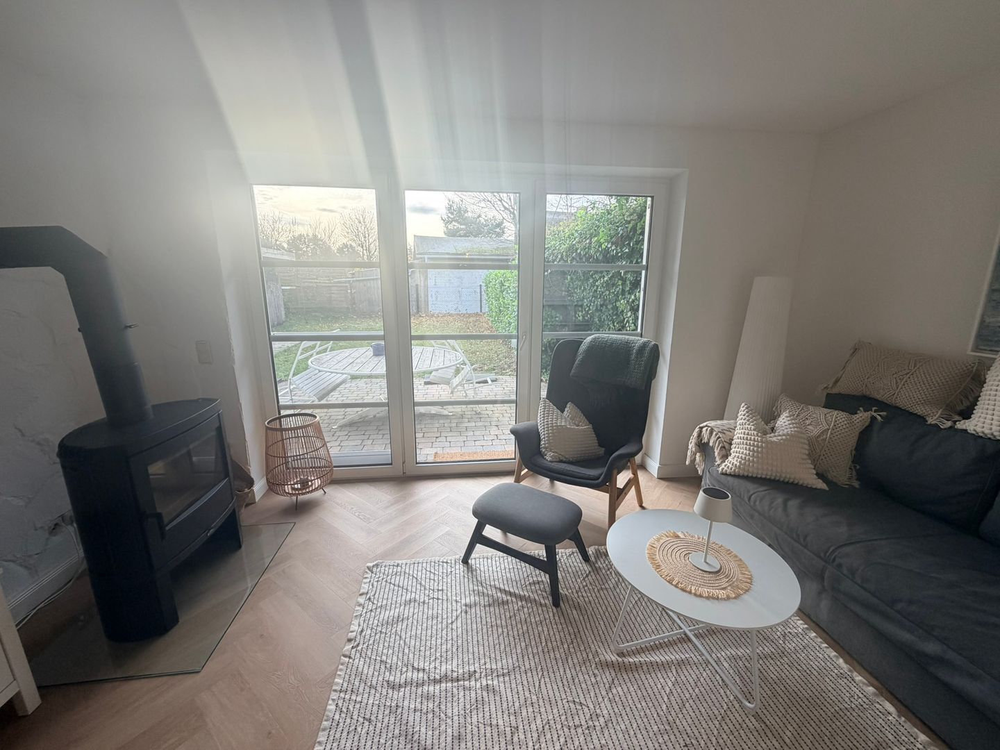 Un salon comprenant un canapé, un fauteuil, une petite table, une cheminée et une vue sur l’extérieur, visible à travers une porte vitrée.