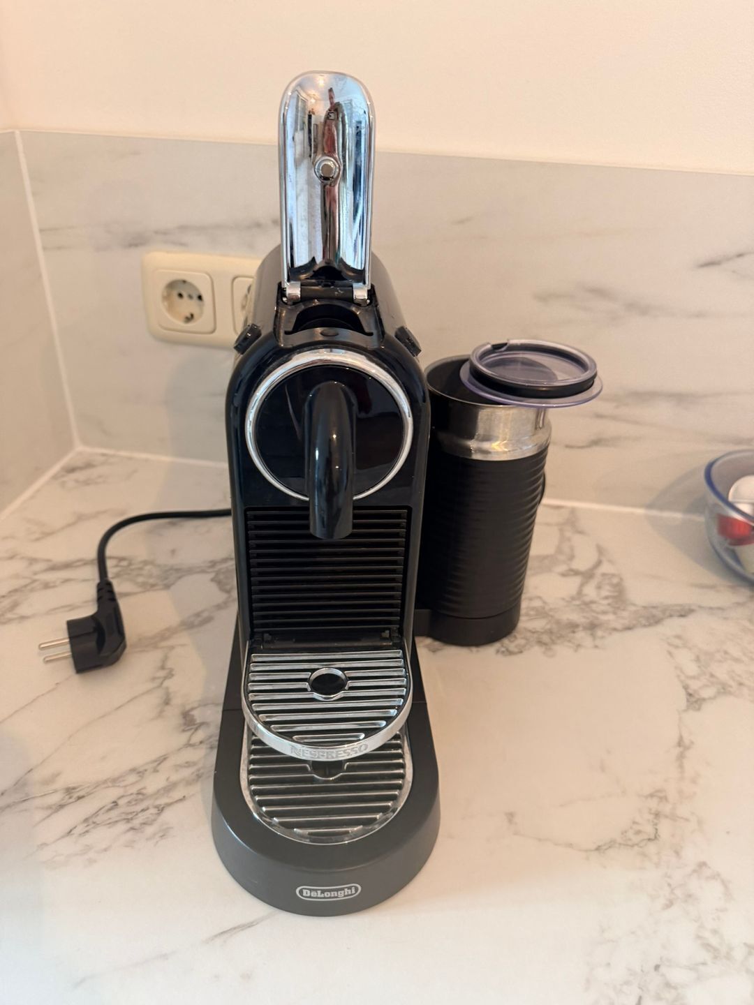 A coffee machine with a power cord, a coffee pot, and a container on a marble countertop.