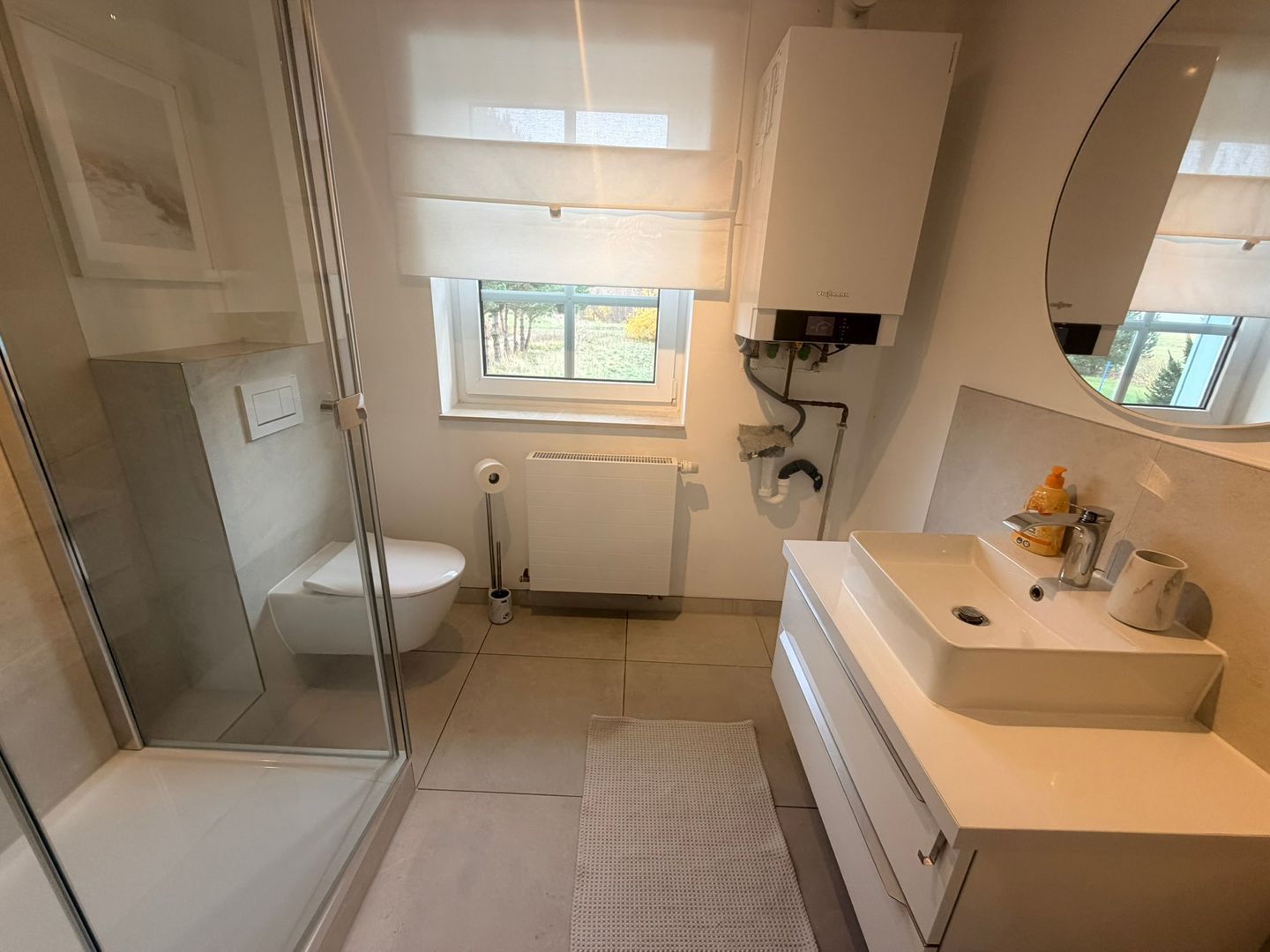 Et stilfuldt badeværelse med en glas brusekabine, toilet, vask med spejl og et vindue med naturligt lys.