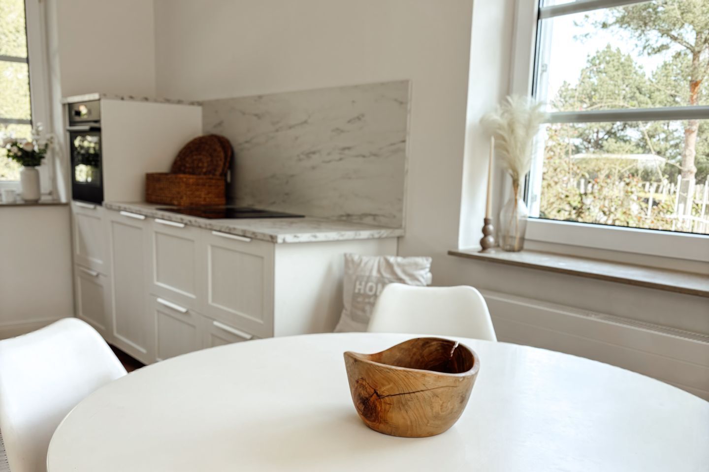 A kitchen with white cabinets, a marble backsplash, and a window with a view of trees.