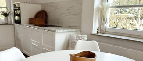 Una cocina con armarios blancos, salpicadero de mármol y ventana con vista a árboles.