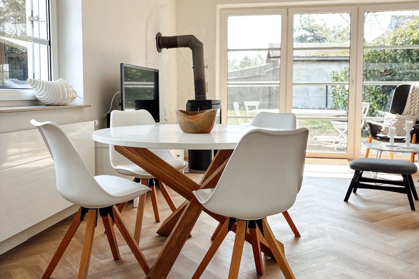 Un comedor moderno con una mesa redonda, sillas blancas y suelo de madera.