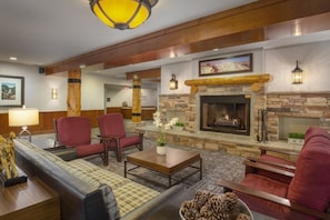 A lobby with a stone fireplace, red chairs, a sofa, and a coffee table.