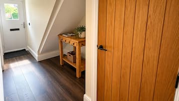 Une porte en bois avec une poignée noire, une console en bois sur laquelle sont posés un panier et une plante, et un plancher en bois foncé.