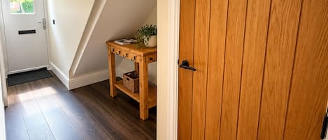 A wooden door with a black handle, a wooden console table with a basket and a plant, and a dark wooden floor.