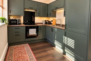 A kitchen with grey cabinets, a microwave, an oven, a sink, and a wooden countertop.