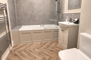 Un baño con bañera, ducha, lavamanos e inodoro.