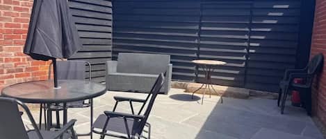 Een terras buiten met een ronde tafel, twee stoelen, een klein rond tafeltje en een parasol.