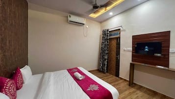 A hotel room with a bed, a TV mounted on the wall, a ceiling fan, and a window with curtains.