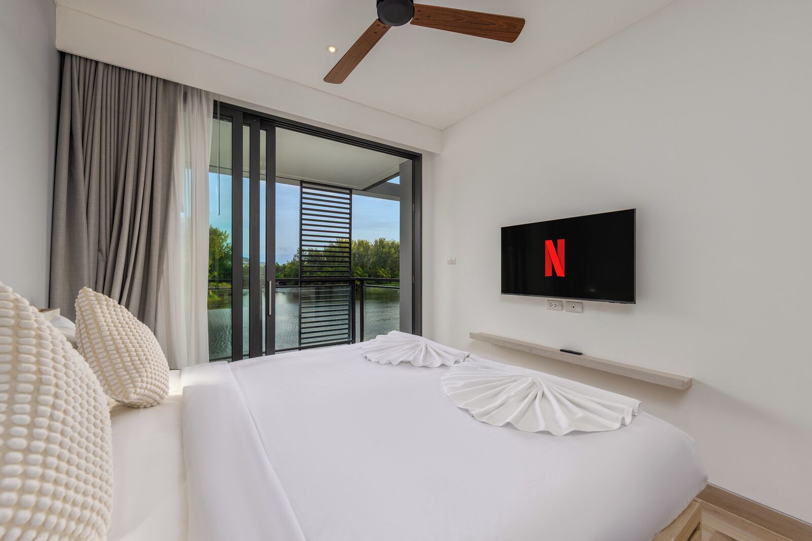 Quarto de hotel com cama, televisão fixada na parede e vista do exterior por uma porta de correr.