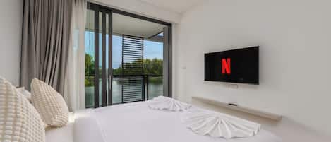 A hotel room with a bed, a television mounted on the wall, and a view of the outdoors through a sliding door.