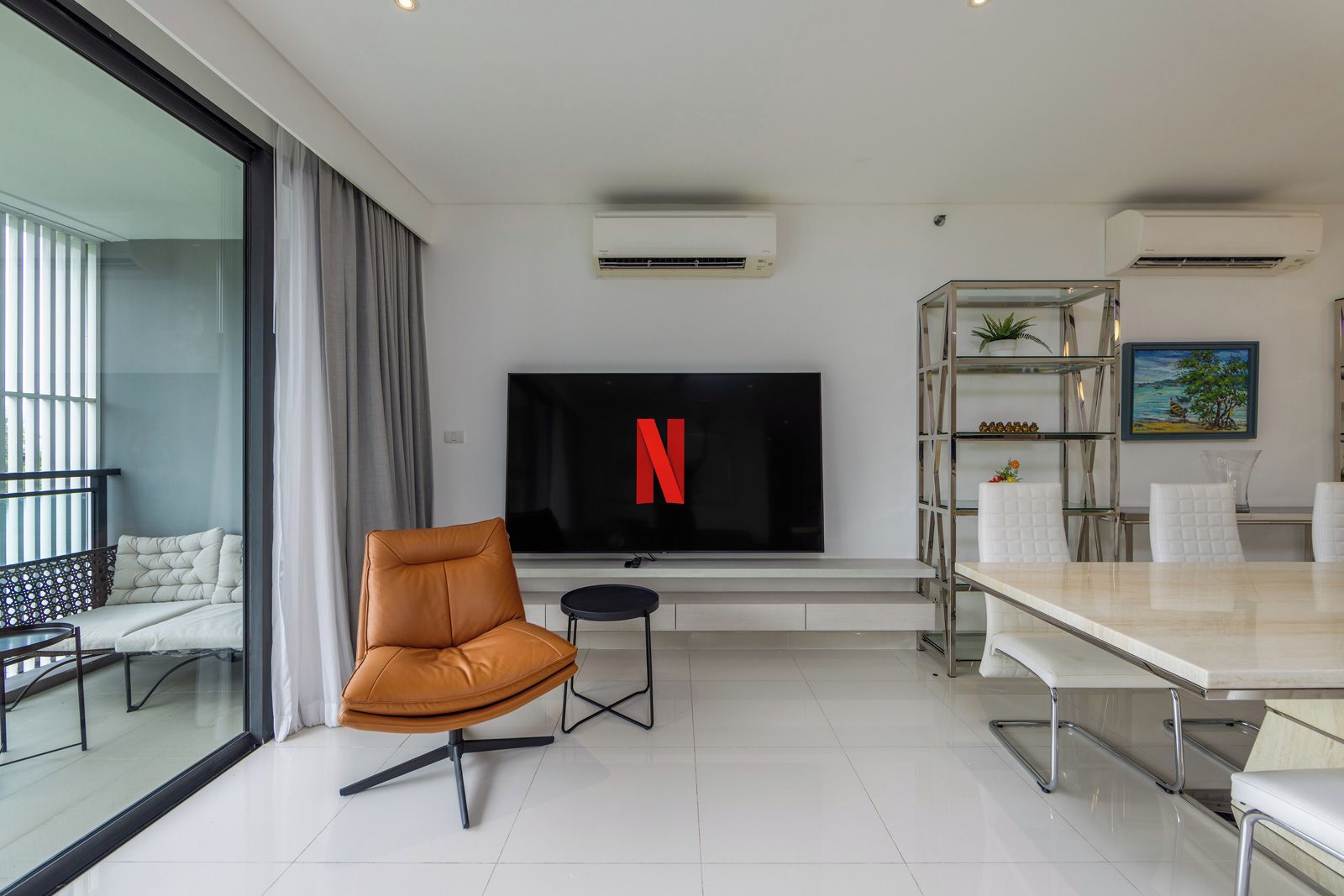 A modern living room with a flat-screen TV, a sofa, a dining table, and a glass partition.