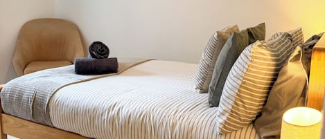 Un letto singolo con struttura in legno, una testiera e un comodino con una lampada.
