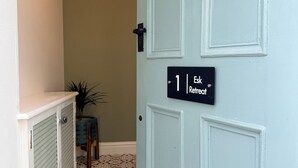 A hallway with a patterned floor, a door labeled '1 Esk Retreat', and a small plant.