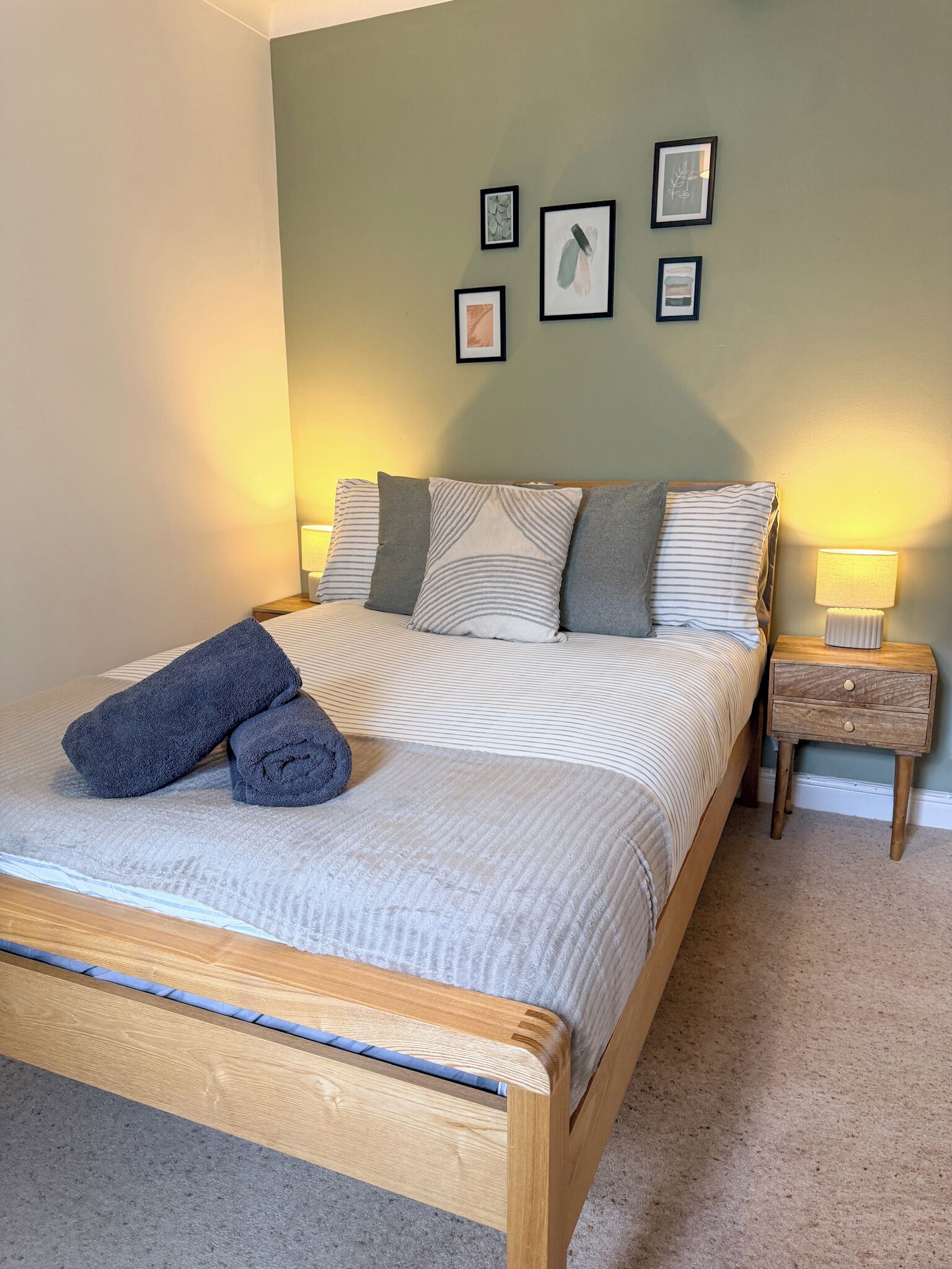 A neatly made bed with a striped bedspread and pillows, a wooden headboard, and a nightstand with a lamp.
