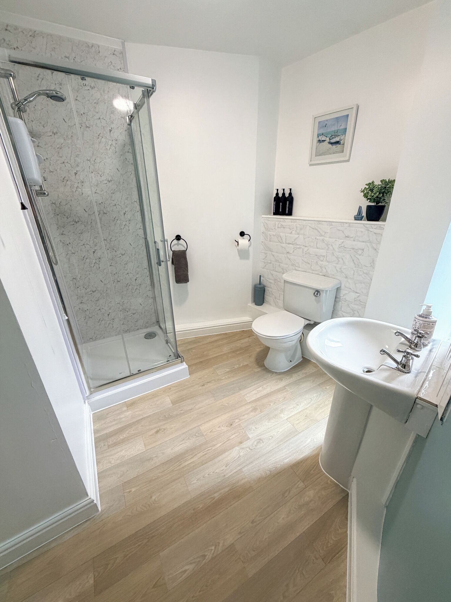 A bathroom with a glass shower enclosure, a toilet, a sink, and a marble-tiled wall.