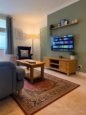 Een woonkamer met een aan de muur bevestigde televisie, een bank, een salontafel en een vloerkleed.