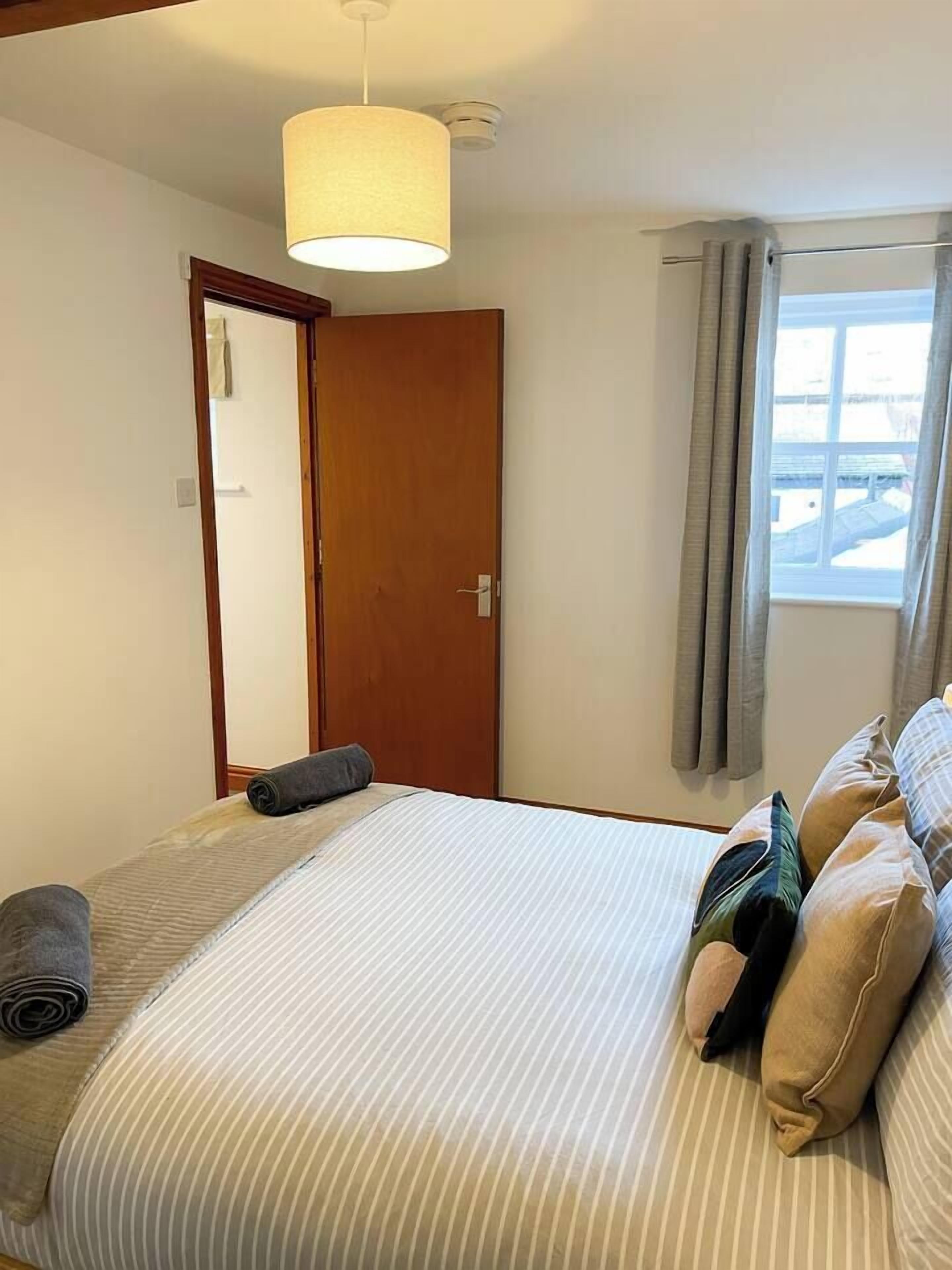 Ein Schlafzimmer mit einem Bett, einer Tür, einem Fenster mit Vorhängen und einer Pendelleuchte.