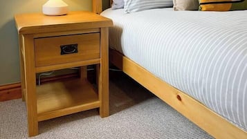 Een slaapkamer met een houten nachtkastje, een lamp, een bed met gestreepte beddengoed en ingelijste foto's aan de muur.