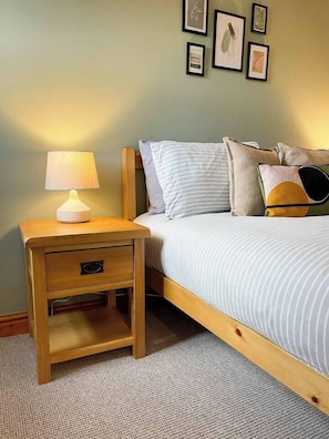 Quarto com mesa de cabeceira de madeira, luminária, cama com roupa de cama listrada e quadros na parede.