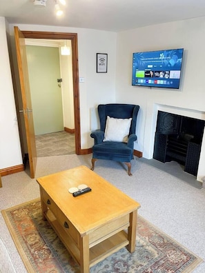 Sala de estar com mesa de centro de madeira, poltrona azul, lareira e televisão na parede exibindo a tela inicial.
