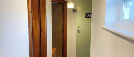 Un pasillo estrecho con puertas de madera, un aplique colgante y una ventana con persiana.