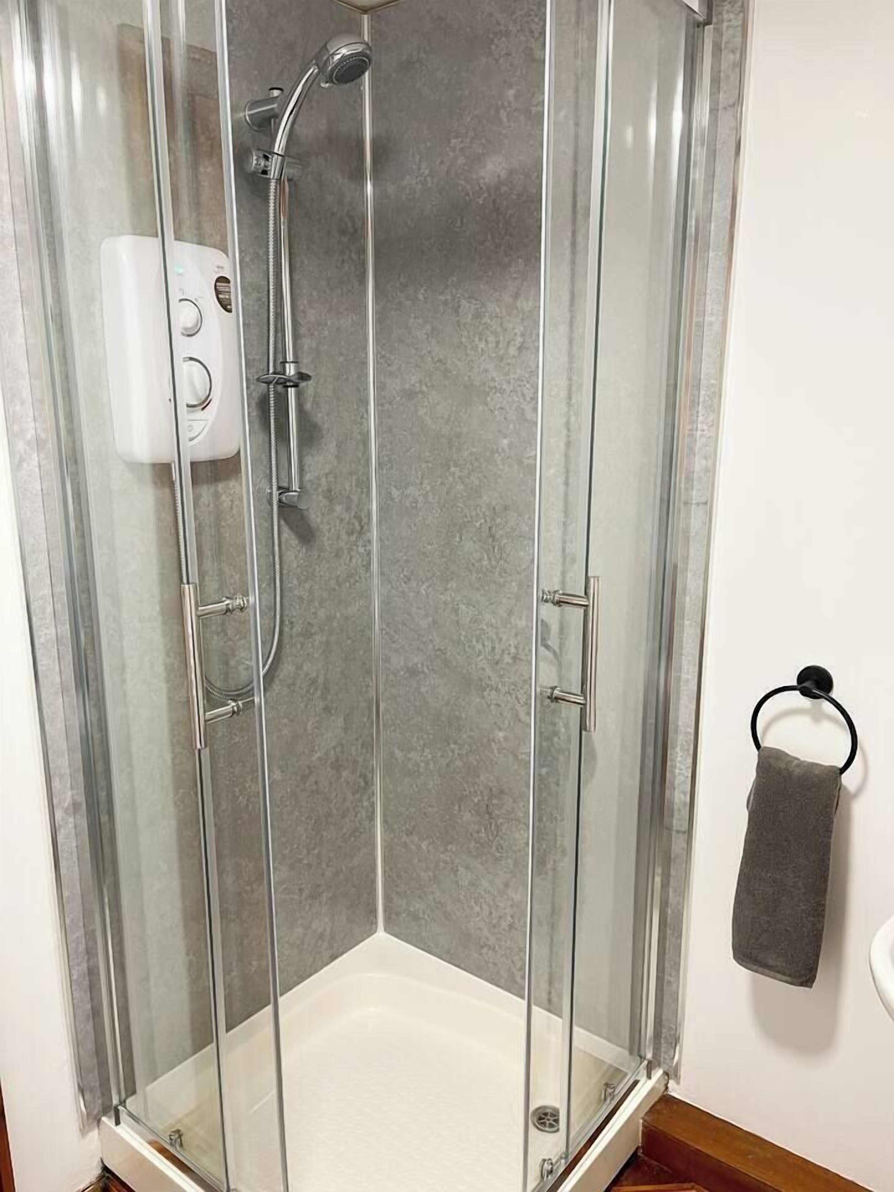 A glass-enclosed shower stall with a handheld showerhead and a wall-mounted control panel.