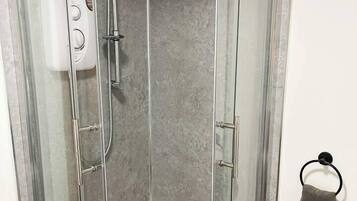 A glass-enclosed shower stall with a handheld showerhead and a wall-mounted control panel.