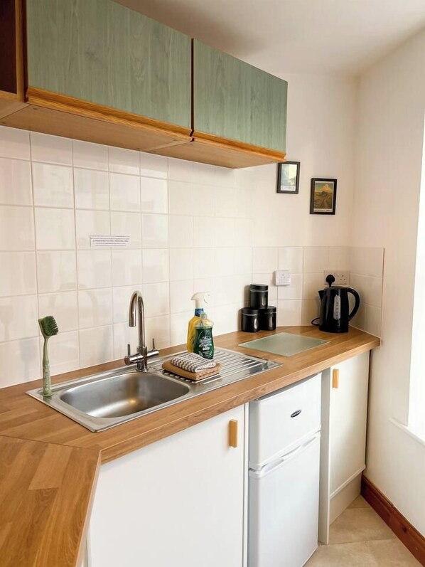 A compact kitchen with a sink, a coffee maker, and a small refrigerator.