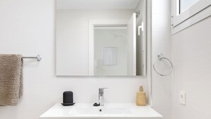 Een moderne badkamer met een witte wastafel, een spiegel, een handdoekrek en een prullenbak.