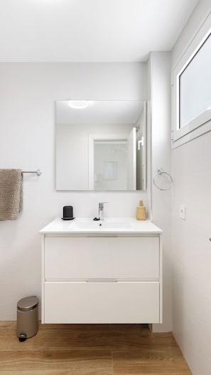 A modern bathroom with a white vanity, a mirror, a towel rack, and a trash can.