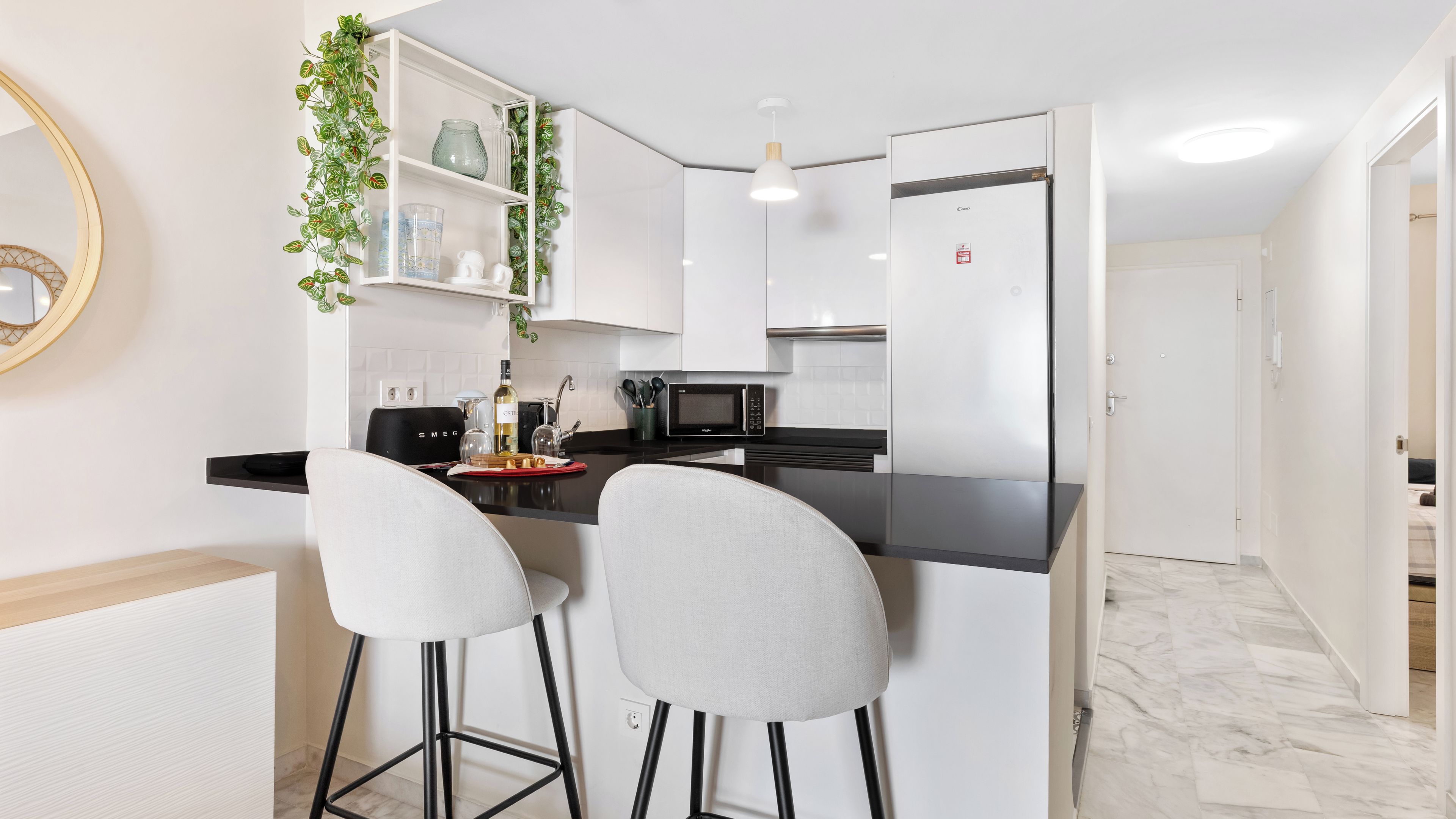 Una cocina moderna con gabinetes blancos, encimera negra y dos taburetes de bar.