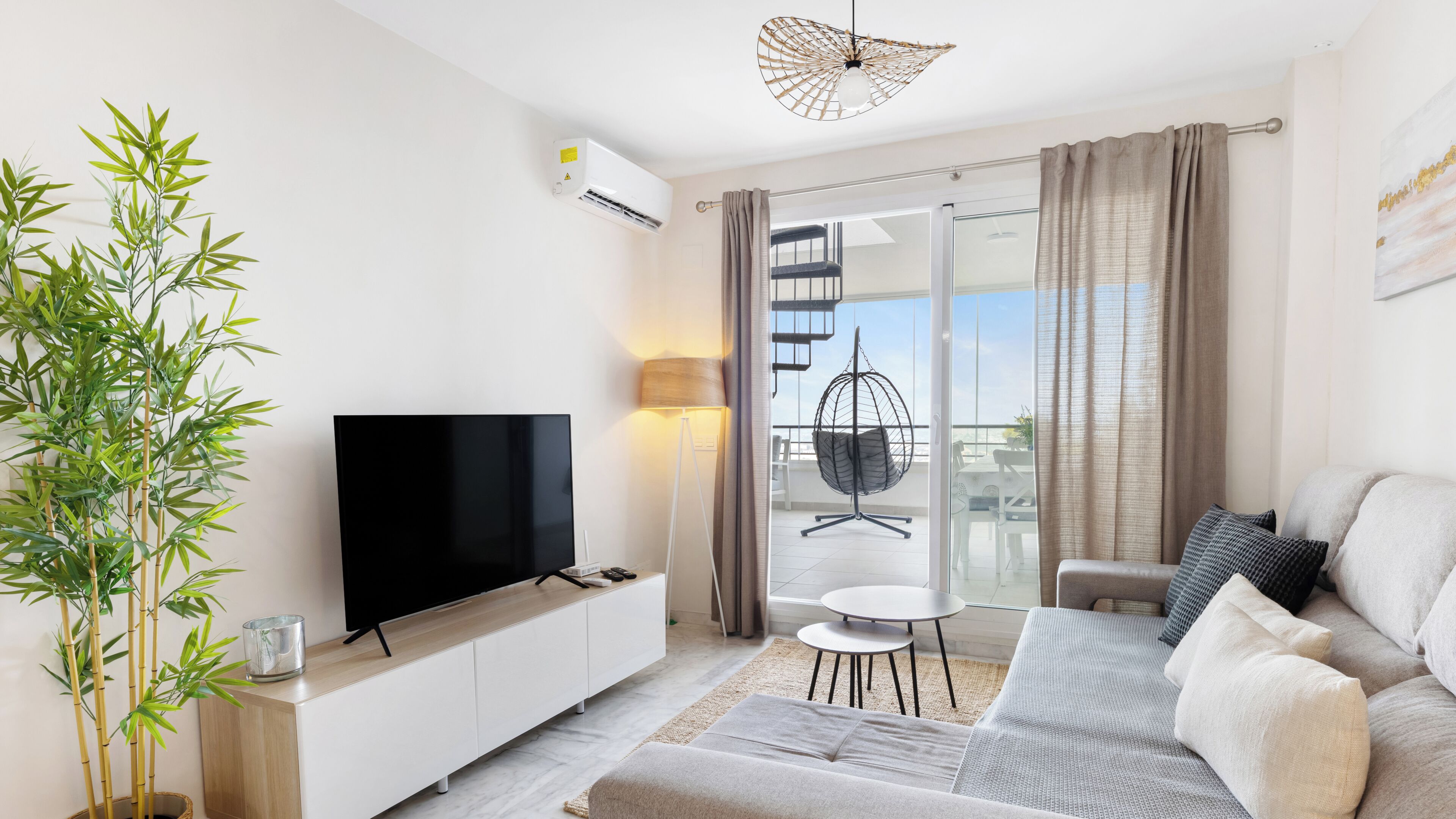 Una sala de estar moderna con televisor de pantalla plana, un sofá, una mesa de comedor y un sillón colgante.