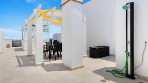 A rooftop terrace with a table and chairs, a black storage box, and a water fountain.