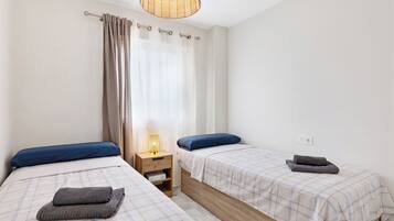 Un dormitorio con dos camas, una mesita de noche, una lámpara y una ventana con cortinas.