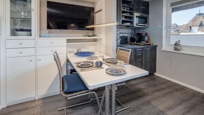Una cucina moderna con mobili bianchi, un tavolo da pranzo apparecchiato con piatti blu e bianchi e un grande televisore a schermo piatto sopra il bancone.
