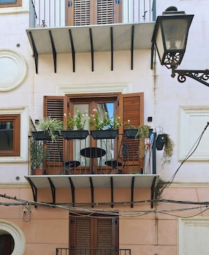 A balcony with wooden shutters, potted plants, and a metal railing. - Domus 16 - Boutique Sicilian Stay (Palermo)