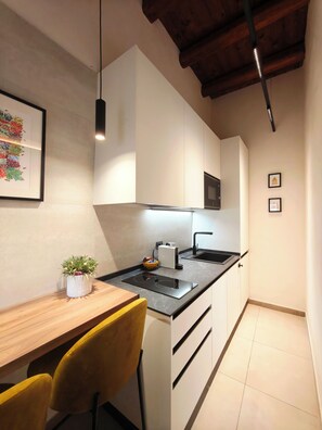 A modern kitchen with a black countertop, white cabinets, a wooden dining table, and yellow chairs. - Domus 16 - Boutique Sicilian Stay (Palermo)