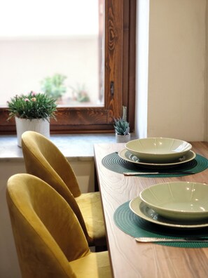 A dining table with green placemats, a set of plates, and a potted plant on the windowsill. - Domus 16 - Boutique Sicilian Stay (Palermo)