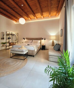 Une chambre à coucher moderne avec un plafond en bois, un grand lit, des tables de chevet, un canapé et une lampe sur pied.