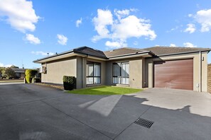 A modern two-story house with a garage, large windows, and a well-maintained lawn. - Avalon: A cosy, modern home that makes being away feel a little easier. (Bairnsdale)